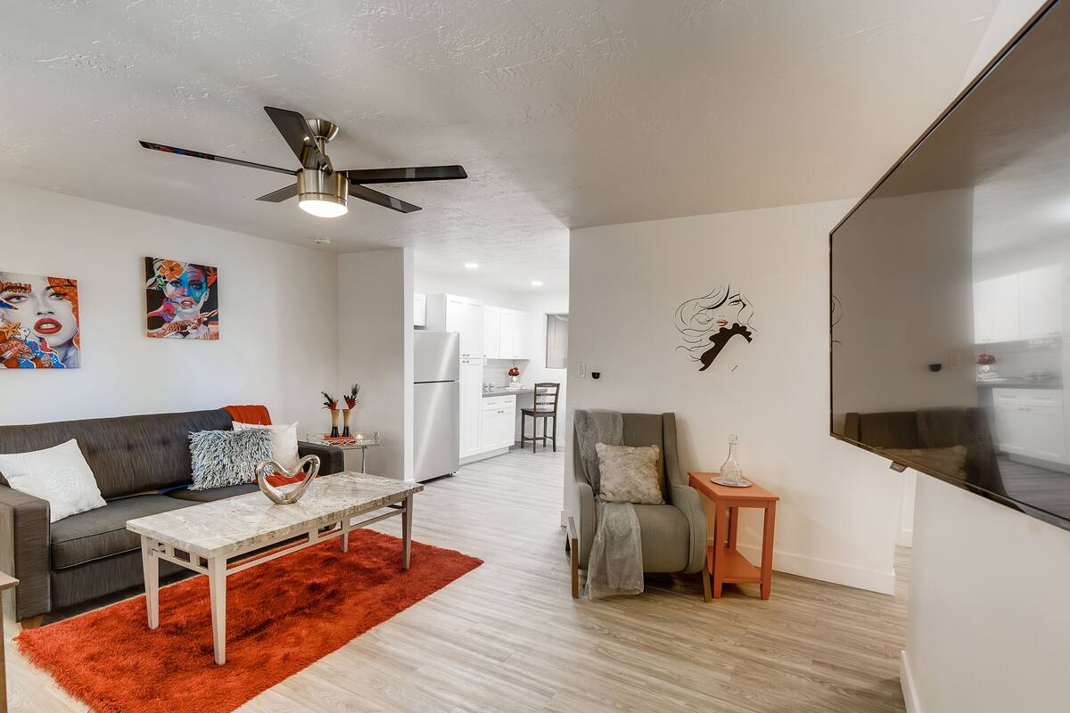 A modern living room with a grey sofa, a coffee table, a red rug, and a ceiling fan.