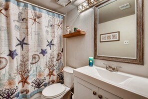 A bathroom with a nautical-themed shower curtain, a white sink with a mirror above it, and a small shelf with decorative items. - The Stars of Old Town (Scottsdale)