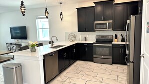 A modern kitchen with dark cabinetry, a stainless steel refrigerator, a microwave, and a dishwasher.