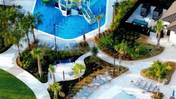 A resort with a large swimming pool, sun loungers, palm trees, and a water slide.