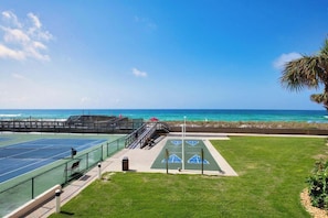 Enjoy a game of tennis on our outdoor court, surrounded by a lush lawn and a palm tree, with the ocean in the background.