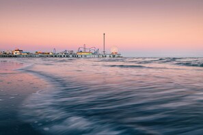 Un muelle se adentra en aguas tranquilas, con una noria y atracciones de feria al fondo.
