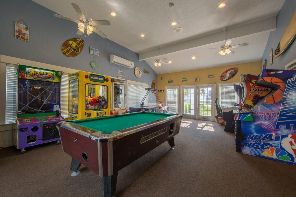 A pool table in a room with arcade games, ceiling fans, and sports memorabilia.