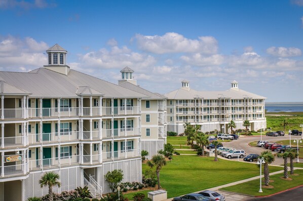 A multi-story hotel with balconies, a parking lot, and a view of the ocean.