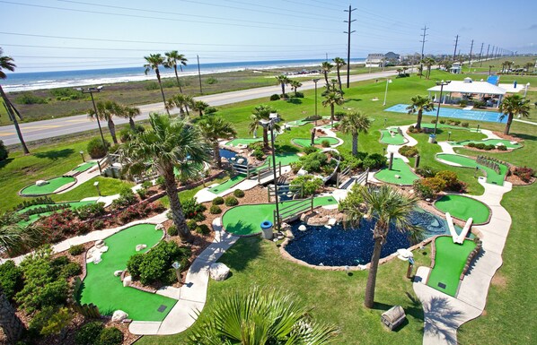 A golf course with multiple greens, a pond, and a view of the ocean.