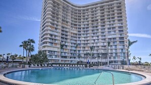A high-rise hotel with a pool area, multiple balconies, and palm trees.