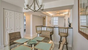 A dining area with a glass table, wicker chairs, and a chandelier.