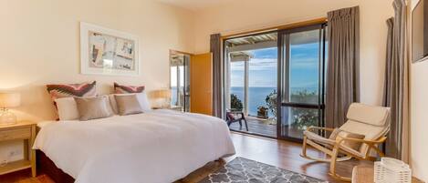 Quarto com cama grande, uma cadeira, vista para o mar e varanda.