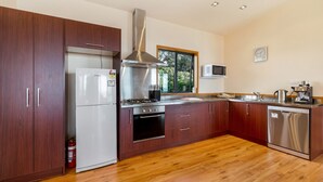 A modern kitchen with wooden cabinets, stainless steel appliances, and a window providing natural light. - Moeraki (Waiheke Island)
