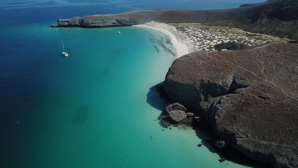 An aerial view of a coastal area with clear turquoise waters, a sandy beach, and rocky terrain. - The ultimate sailing yacht vacation in the Sea of Cortez. Jersey Girl II  (La Paz)