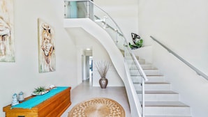 Un interior moderno con una escalera curva, una consola de madera y un tapete redondo.