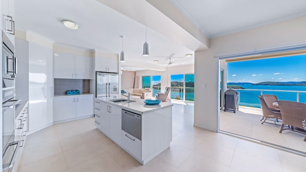 Cocina moderna con alacenas blancas, lavavajillas y una isla grande. Tiene un balcón con vista al mar.