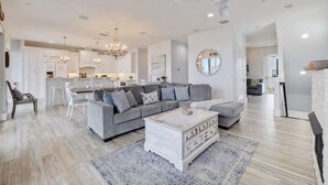 A spacious living room with a grey sectional sofa, a white coffee table, and a chandelier.
