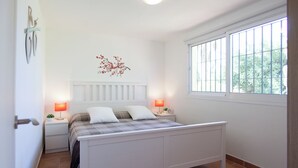 A bedroom with a bed, two bedside tables, a wall-mounted light fixture, a window with bars, and a decorative wall piece. - Private Holiday Home in the Countryside (Alhaurín el Grande)