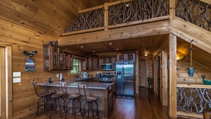 A wooden cabin interior with a kitchen area featuring a central island, bar stools, and a refrigerator. - A View  To Remember (Morganton)