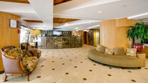 A lobby with a reception desk, a sofa, a chair, and a large potted plant. - 10th Floor Air Conditioned Apt in Central -Bamboo Waikiki 1005 (Honolulu)