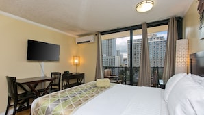 A hotel room with a large bed, a desk with chairs, a flat-screen TV, an air conditioning unit, and a balcony with a city view. - 10th Floor Air Conditioned Apt in Central -Bamboo Waikiki 1005 (Honolulu)