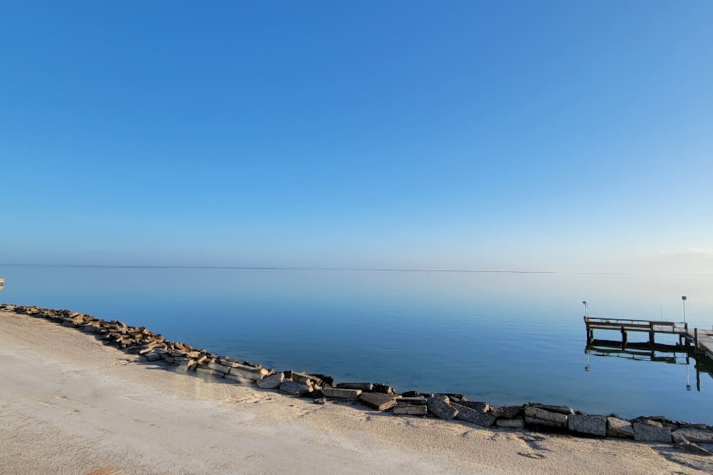 En stilla sjö med en träbrygga som sträcker sig ut i vattnet, omgiven av en stenig strand.