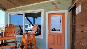 En træterrasse med to Adirondack-stole, en lille skammel, en dør med et vindue og en velkomst måtte.