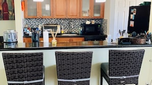 Una cocina con armarios de madera, un refrigerador negro y una zona de bar con sillas de mimbre.
