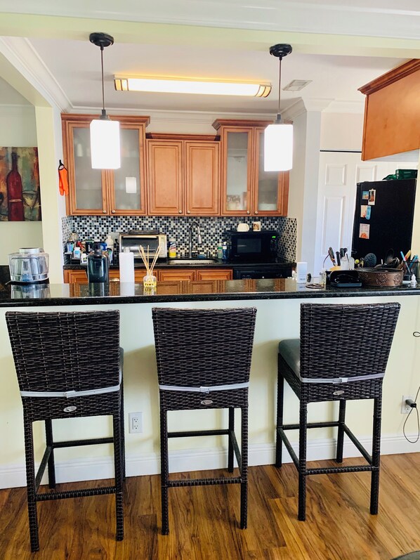 A kitchen with wooden cabinets, a black refrigerator, and a bar area with wicker chairs.
