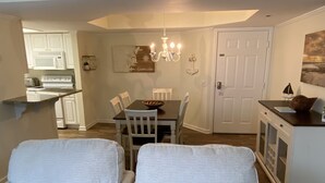 A dining area with a table and chairs, a chandelier, and a kitchen in the background. - Top Floor, Partial Oceanview, Peaceful Condo (St. Simons)