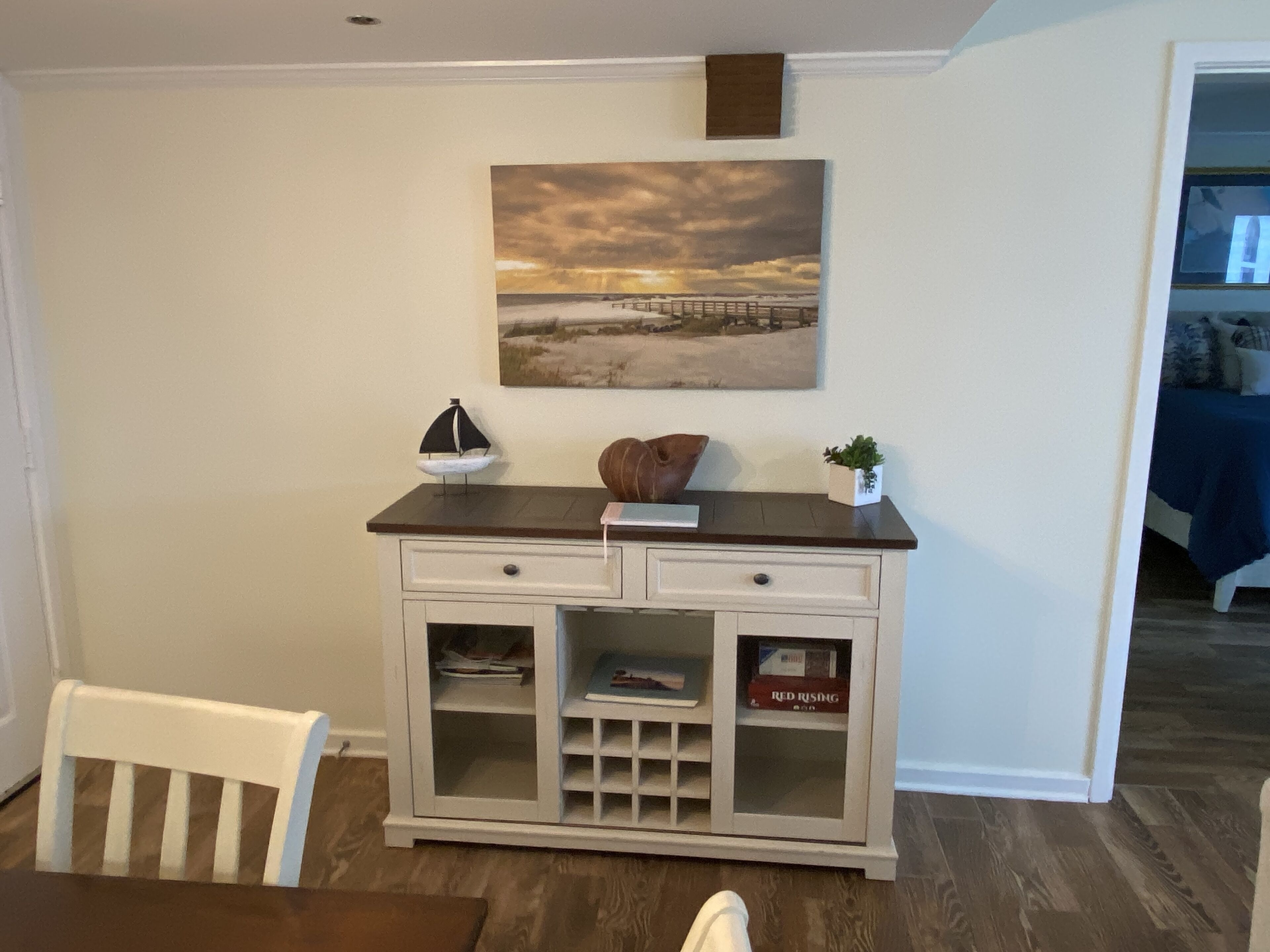 A dining area with a white cabinet, a painting of a sunset, and a small sailboat model.