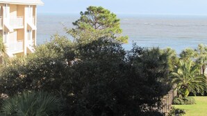 A building with a balcony overlooking a body of water, surrounded by dense foliage and palm trees. - Top Floor, Partial Oceanview, Peaceful Condo (St. Simons)