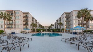 A pool area with lounge chairs and umbrellas, surrounded by multi-story buildings with balconies. - Top Floor, Partial Oceanview, Peaceful Condo (St. Simons)