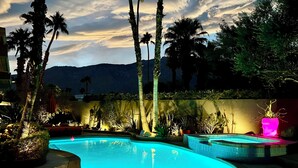 Una piscina con un cerchio gonfiabile verde, circondata da palme e piante, con vista sulle montagne sullo sfondo.