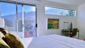 Camera da letto con un ampio letto, una scrivania con sedia, un quadro e vista sulle montagne dalla finestra.