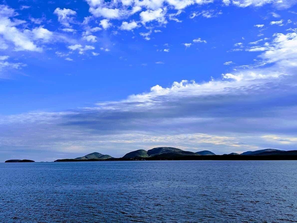 Ein ruhiges Meer mit weit entfernten Landformen unter einem teils bewölkten Himmel.