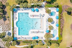 An aerial view of a resort with a large rectangular swimming pool, multiple sun loungers, and umbrellas.