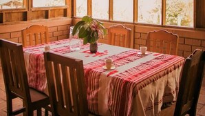 Comedor con una mesa lista para cuatro personas, rodeada de sillas de madera, bajo un techo de madera con un diseño ondulado.
