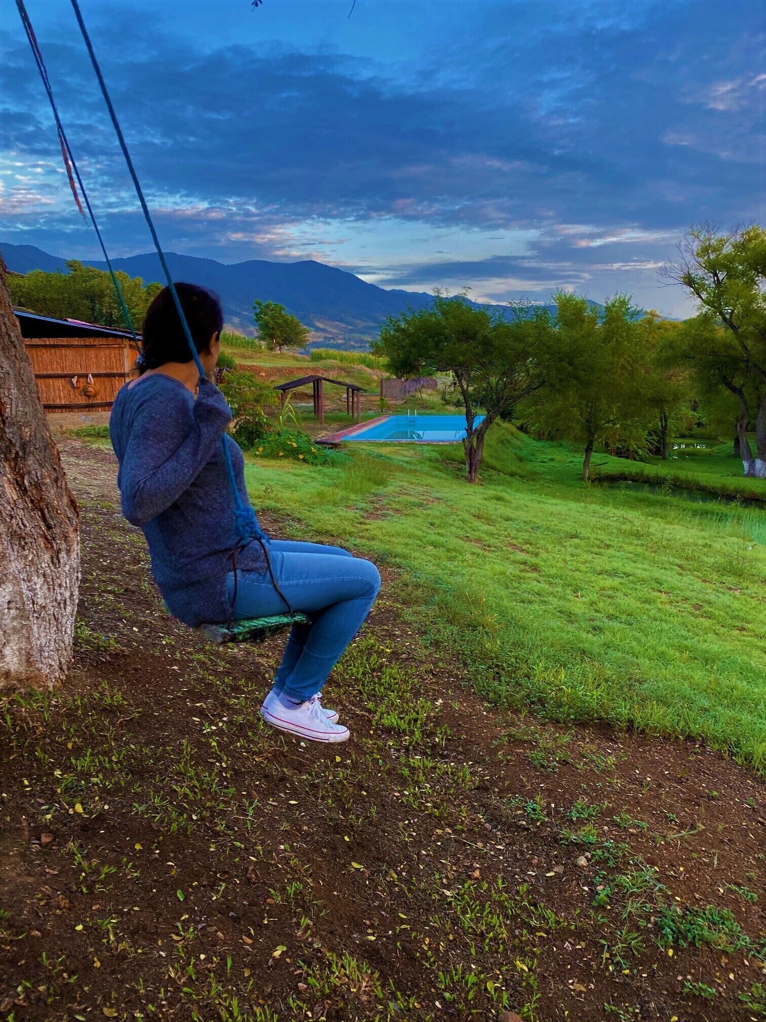 Una persona sentada en un columpio con vista a una piscina y un paisaje montañoso.