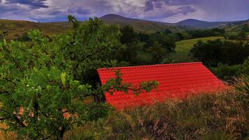 A red-roofed building surrounded by lush greenery and hills in the background.