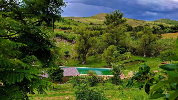 Un paisaje verde y exuberante con una piscina rodeada de árboles y colinas.