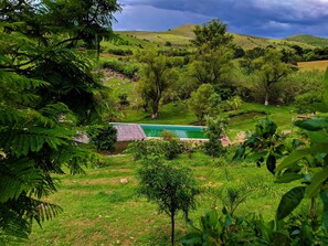 A lush green landscape with a swimming pool surrounded by trees and hills.