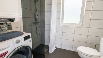Une petite salle de bain équipée d’un lave-linge, d’une douche et de toilettes.