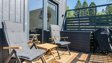 Un espace extérieur aménagé avec deux chaises et une table, un barbecue, et une vue sur une terrasse en bois et des arbres.