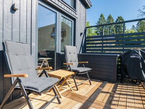 Un espace extérieur aménagé avec deux chaises et une table, un barbecue, et une vue sur une terrasse en bois et des arbres.