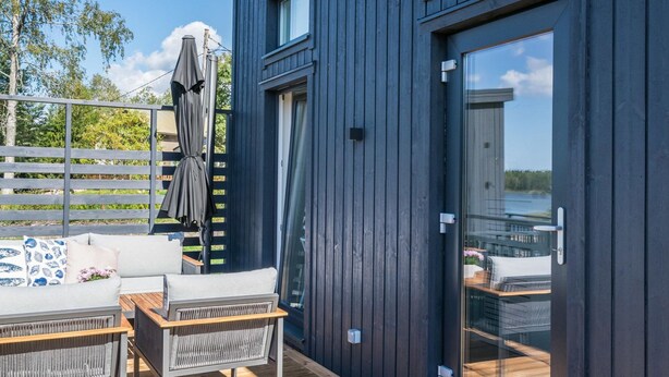 Una terraza moderna al aire libre con un sofá, sillas, una mesa de madera y un amplio ventanal corredera.
