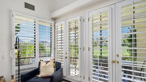 A room with a dark blue sofa, a lamp, and a view of a green landscape through white-framed glass doors. - Golf Course Retreat w/ Private Casita Steps to La Quinta Resort & Pools (La Quinta)