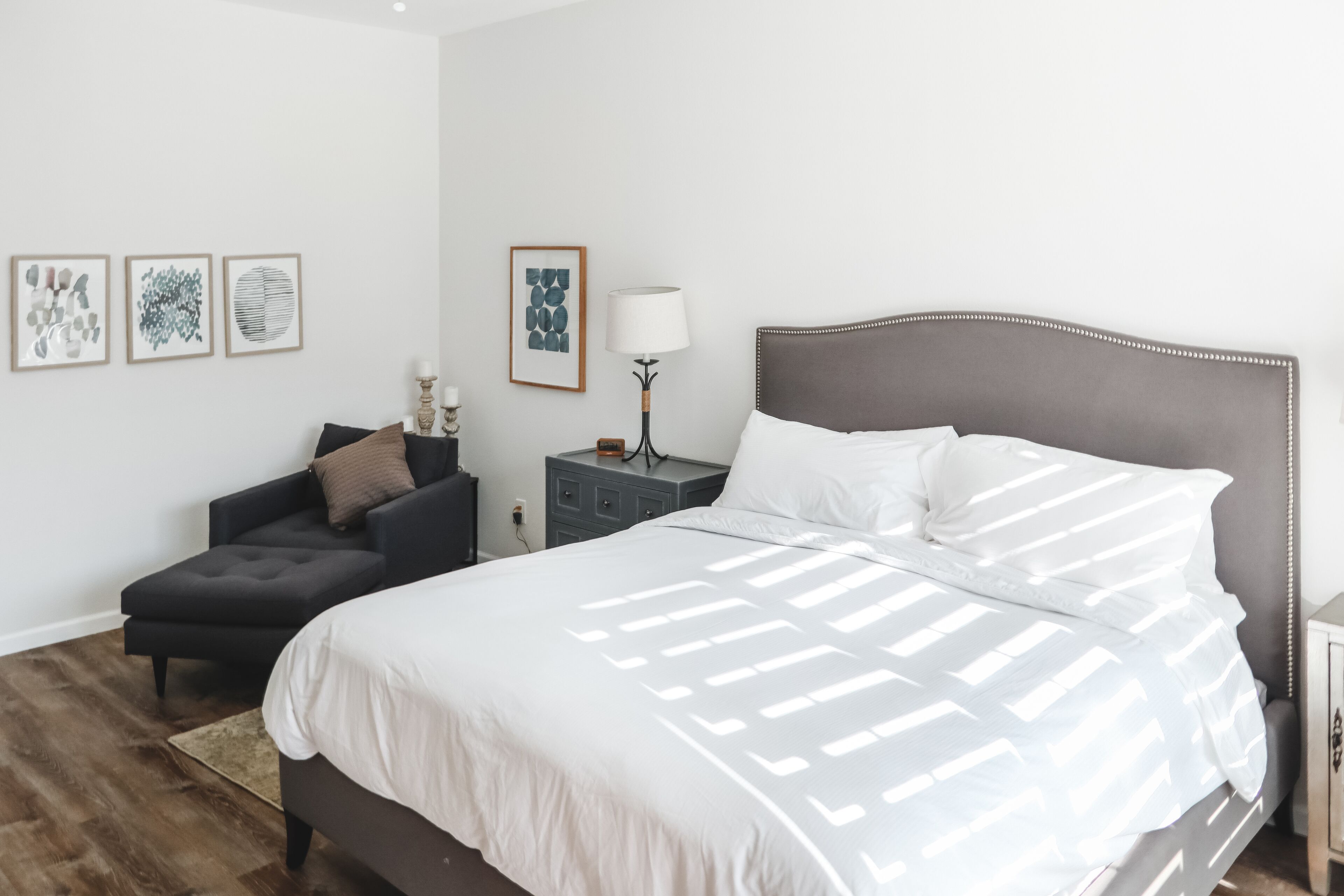 A modern bedroom with a large bed, a small sofa, a bedside table, and wall art.