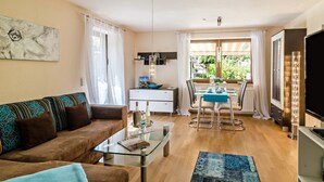 A living room with a sofa, coffee table, and a TV. There is a dining area with a table and chairs. - Comfortable 4-Star Vacation Apartment "Wolf" with Terrace, Grill & Wi-Fi (Überlingen)