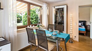 A dining area with a glass table, wicker chairs, a buffet cabinet, and a view of the garden. - Comfortable 4-Star Vacation Apartment "Wolf" with Terrace, Grill & Wi-Fi (Überlingen)