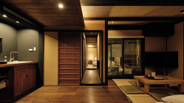A modern interior with a wooden floor, a desk with a computer, a bed with a futon, and a sliding door leading to a bathroom.