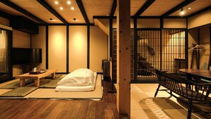 A traditional Japanese-style room with tatami flooring, a low wooden bed, a television, and a sliding door leading to a staircase.