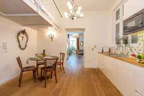 A kitchen with wooden flooring, a dining table with chairs, a chandelier, and a microwave.