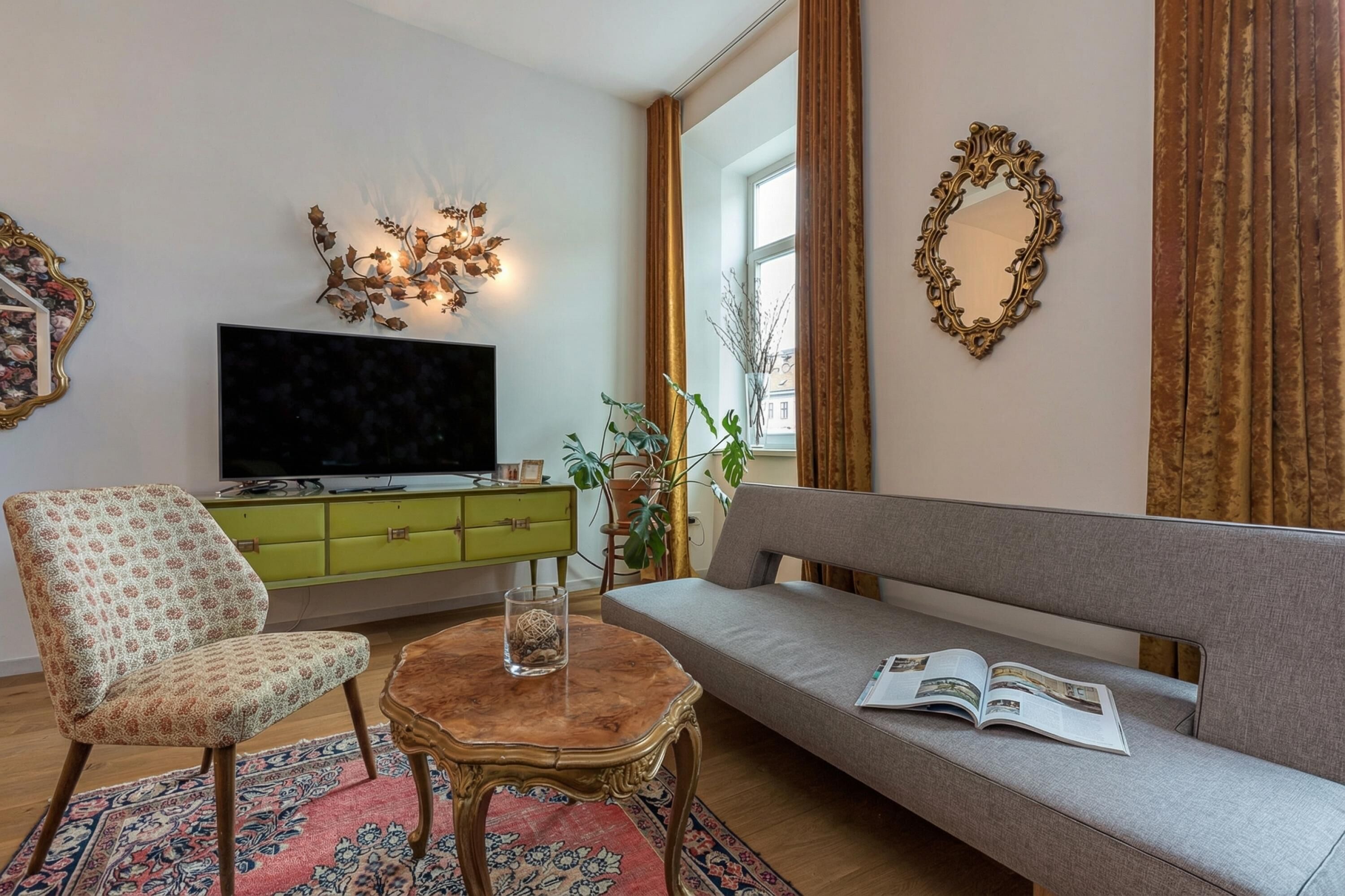 A living room with a sofa, a chair, a coffee table, a TV, a green cabinet, and decorative wall art.